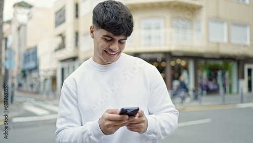 Young hispanic man using smartphone smiling at street