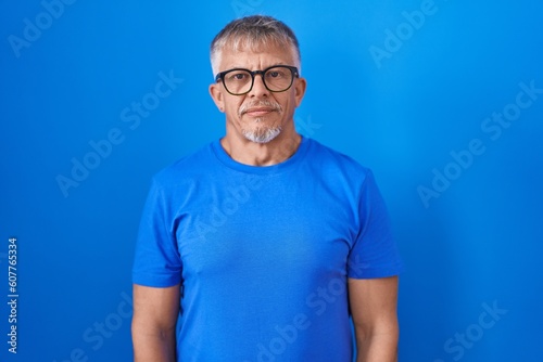 Hispanic man with grey hair standing over blue background relaxed with serious expression on face. simple and natural looking at the camera. © Krakenimages.com