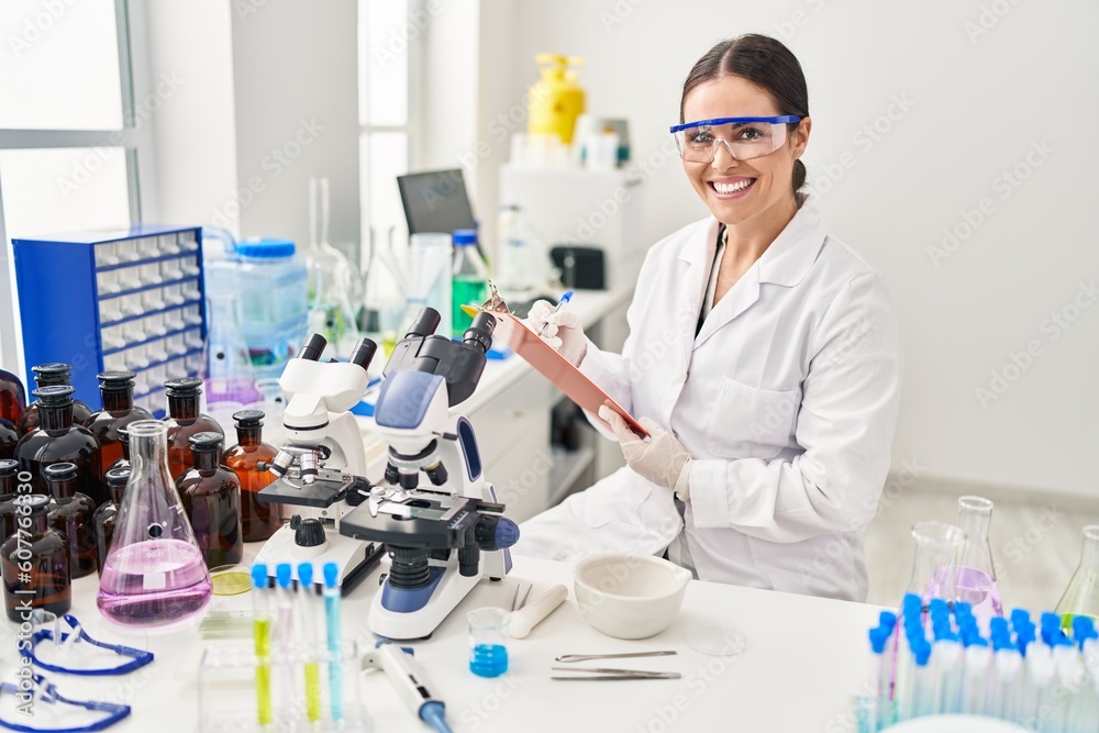 Fototapeta premium Young beautiful hispanic woman scientist smiling confident writing report working at laboratory