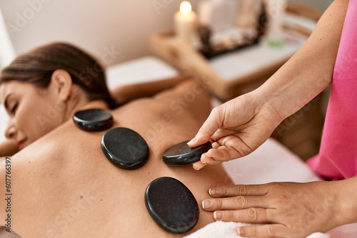 Young beautiful hispanic woman lying on table having hot stones massage at beauty salon