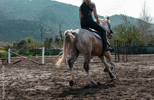 young european girl training horse, riding canter wearing back protection, gray gelding workout in manej
