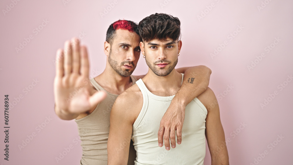 Two men couple doing stop gesture with hand over isolated pink background Two men couple doing stop gesture with hand over isolated pink background