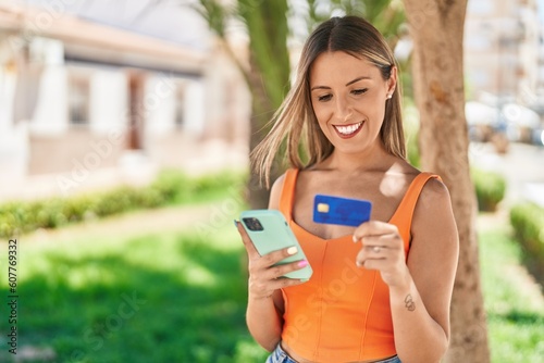 Young beautiful hispanic woman using smartphone and credit card at park