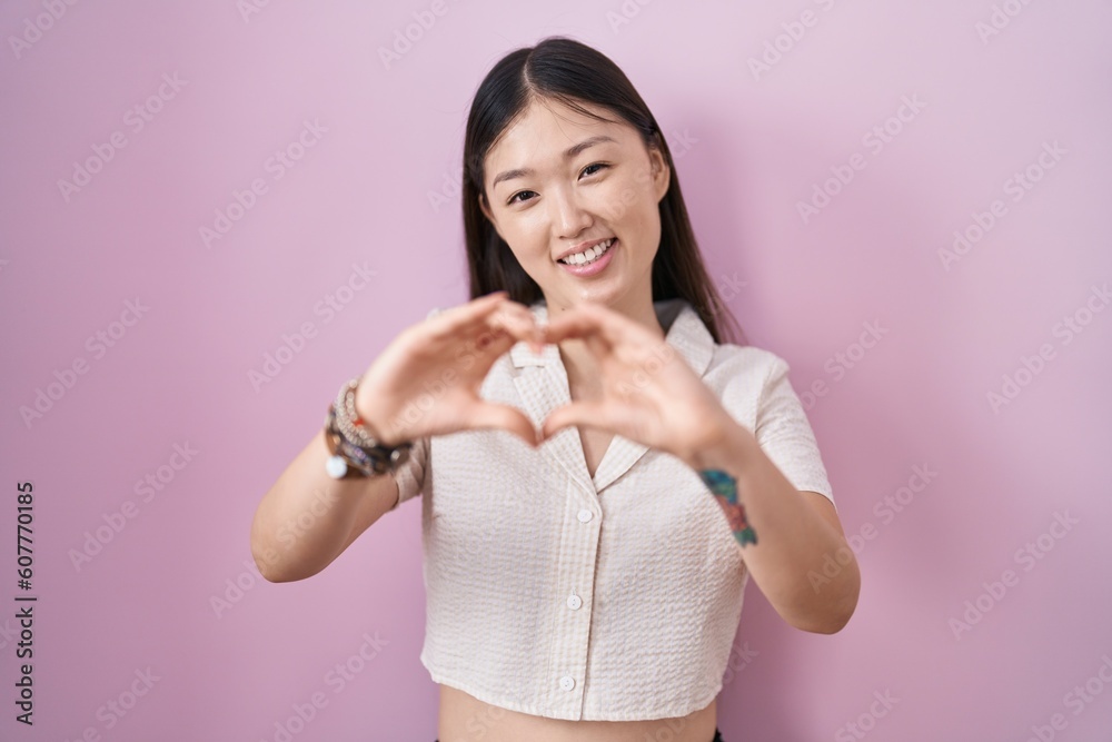Chinese young woman standing over pink background smiling in love doing heart symbol shape with hands. romantic concept. Chinese young woman standing over pink background smiling in love doing heart symbol shape with hands. romantic concept.