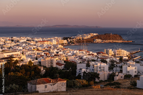 Fototapeta Naklejka Na Ścianę i Meble -  View on the city of Tinos from the hill during sunset. City centre and streets of village of Tinos with white Cycladic houses and Aegean Sea on background, Cyclades, Greece