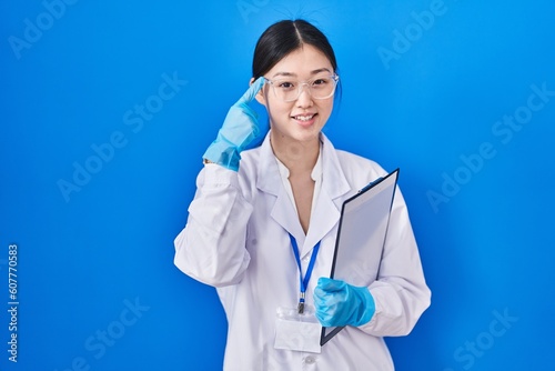 Chinese young woman working at scientist laboratory smiling pointing to head with one finger  great idea or thought  good memory