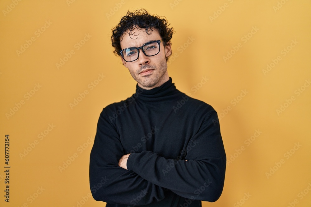 Obraz premium Hispanic man standing over yellow background skeptic and nervous, disapproving expression on face with crossed arms. negative person.