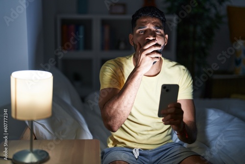 Young arab man using smartphone yawning at bedroom