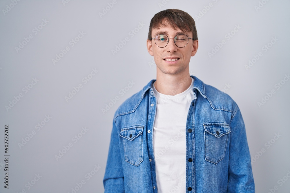 Caucasian blond man standing wearing glasses winking looking at the camera with sexy expression, cheerful and happy face.