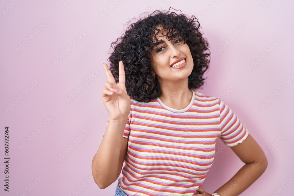 Young middle east woman standing over pink background smiling looking to the camera showing fingers doing victory sign. number two. Young middle east woman standing over pink background smiling looking to the camera showing fingers doing victory sign. number two.