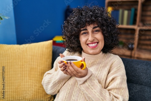 Young middle east woman drinking coffee sitting on sofa at home