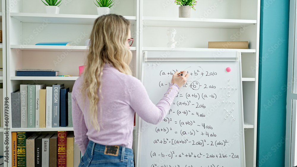 Young blonde woman teacher teaching maths lesson writing on white board at classroom Young blonde woman teacher teaching maths lesson writing on white board at classroom