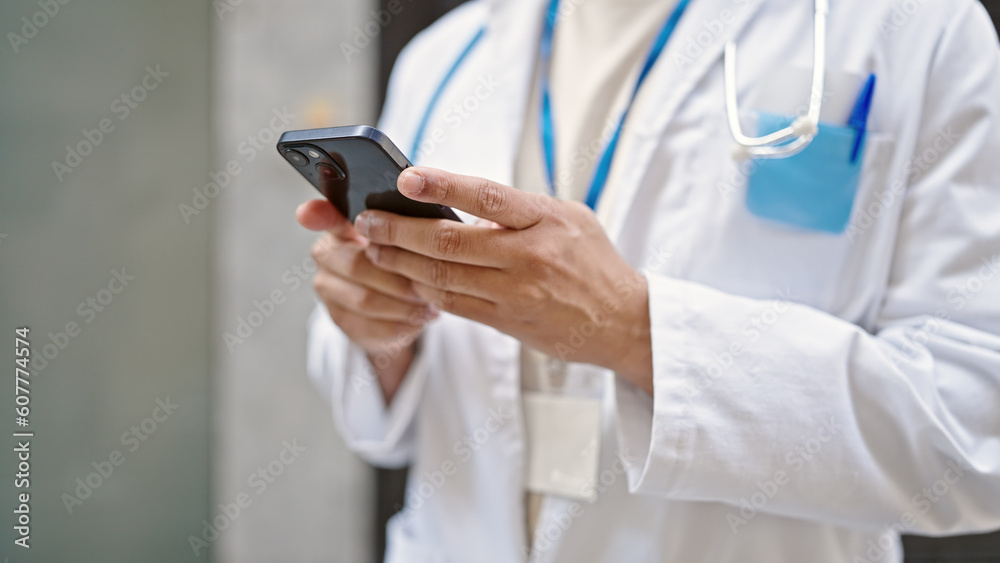 Young latin man doctor using smartphone at street