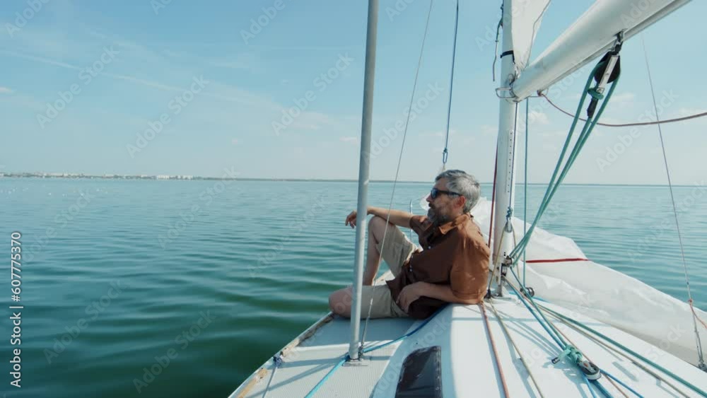 Mature Caucasian man with gray hair and beard on face wearing casual clothes with sunglasses relaxing on yacht on summer day Mature Caucasian man with gray hair and beard on face wearing casual clothes with sunglasses relaxing on yacht on summer day