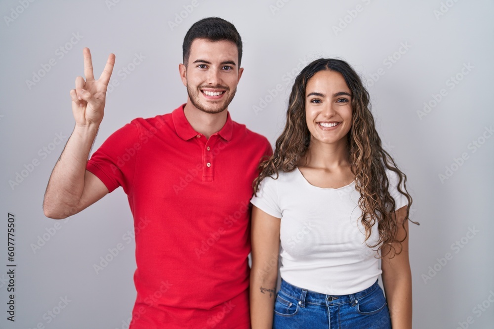 Young hispanic couple standing over isolated background showing and pointing up with fingers number two while smiling confident and happy.
