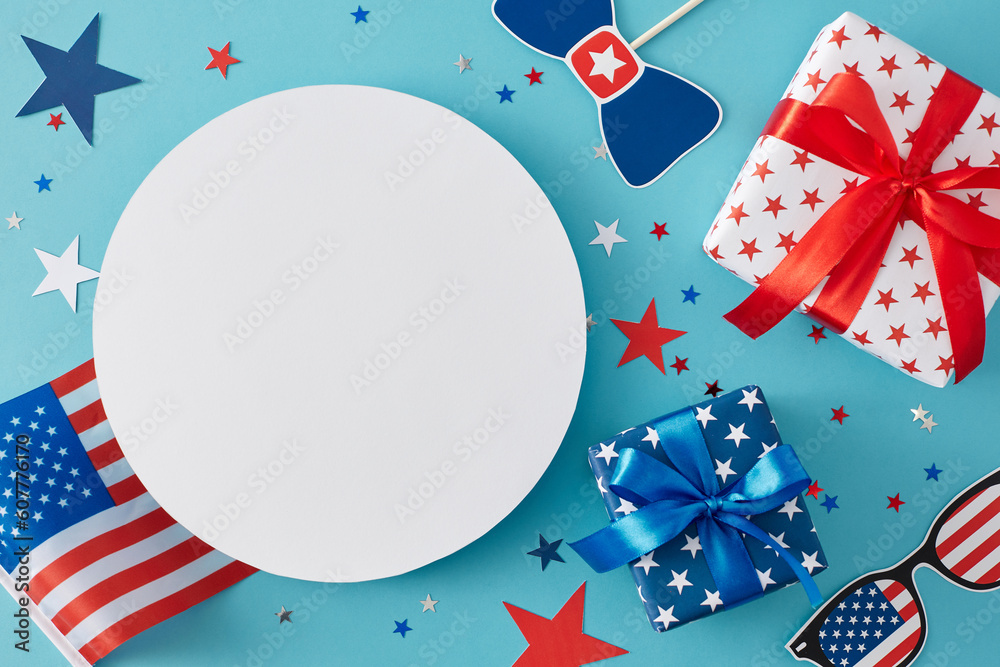 Fototapeta premium Idea for a Fourth of July party. Top view flat lay of gift boxes, american flag, Independence Day supplies, star-shaped confetti on pastel blue background with blank circle for text or advert