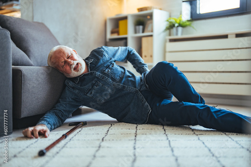 Senior man falling down on carpet and lying on the floor in living room at home, Falls of older adults concept. Senior men with cane falled down on floor at home © Dragana Gordic