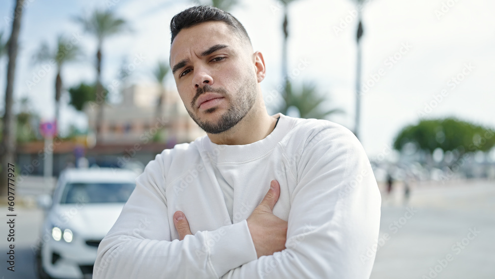 Fototapeta premium Young hispanic man standing with serious expression and arms crossed gesture at street