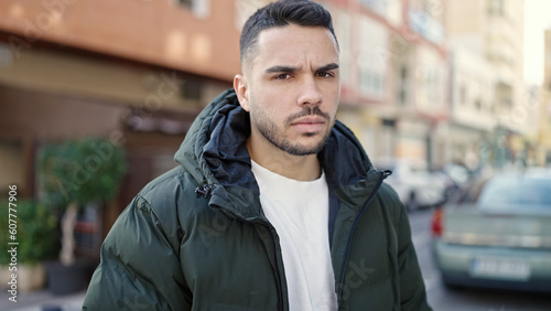 Young hispanic man standing with serious expression at coffee shop terrace