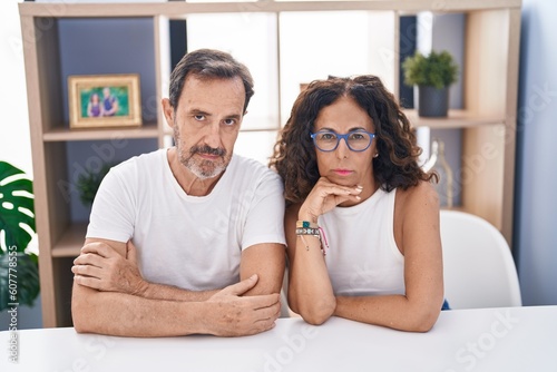 Man and woman couple sitting on table with serious expression at home
