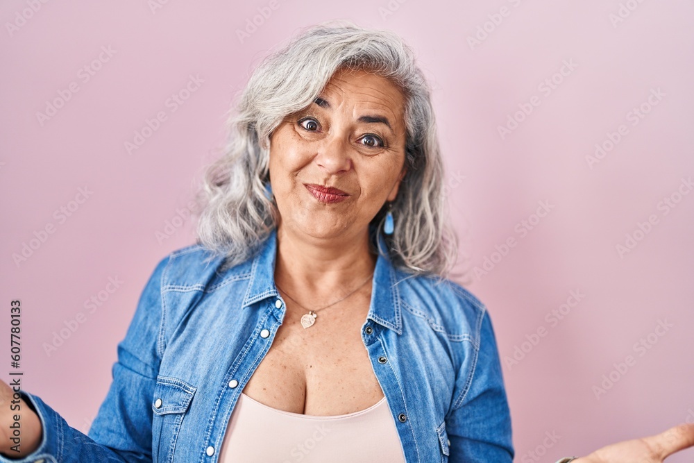 Middle age woman with grey hair standing over pink background smiling cheerful with open arms as friendly welcome, positive and confident greetings Middle age woman with grey hair standing over pink background smiling cheerful with open arms as friendly welcome, positive and confident greetings