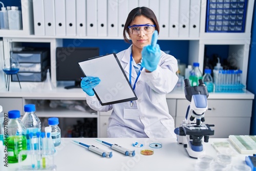 Hispanic young woman working at scientist laboratory showing middle finger  impolite and rude fuck off expression