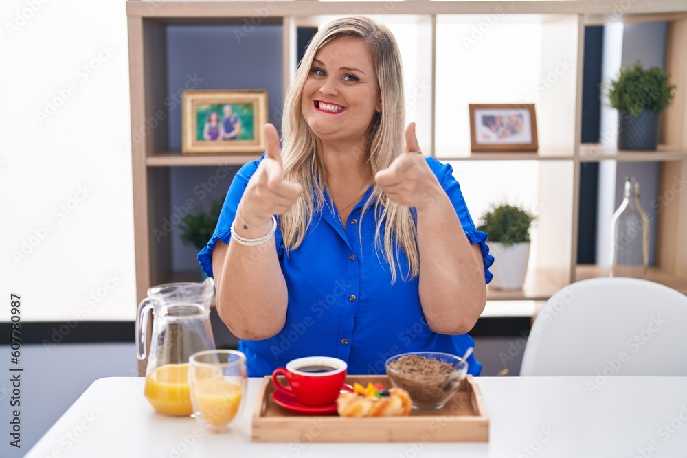 Caucasian plus size woman eating breakfast at home pointing fingers to camera with happy and funny face. good energy and vibes. Caucasian plus size woman eating breakfast at home pointing fingers to camera with happy and funny face. good energy and vibes.