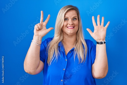 Caucasian plus size woman standing over blue background showing and pointing up with fingers number eight while smiling confident and happy.