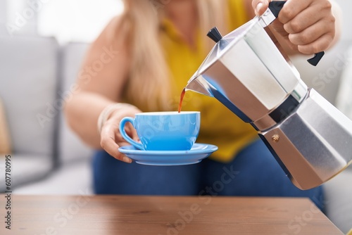 Young woman pouring coffee on cup sitting on sofa at home