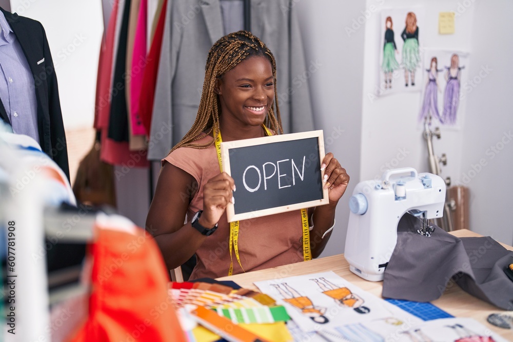 African american woman tailor sitting on table holding open blackboard message at tailor shop