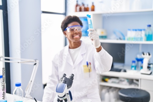 Fototapeta Naklejka Na Ścianę i Meble -  African american woman wearing scientist uniform write on clipboard holding test tubes at laboratory