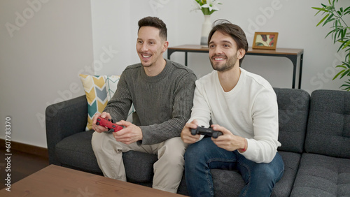 Two men couple sitting on sofa playing video game at home