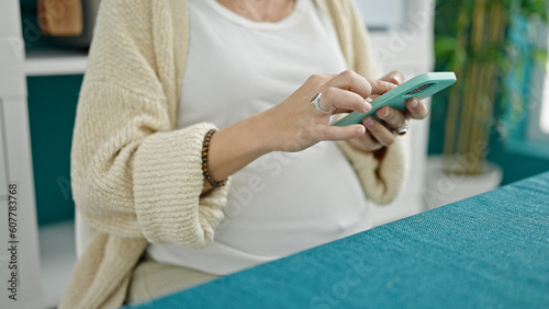 Young pregnant woman using smartphone at dinning room