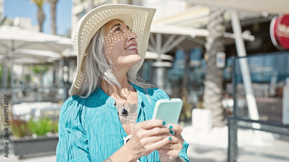 Middle age grey-haired woman tourist smiling confident using smartphone at coffee shop terrace