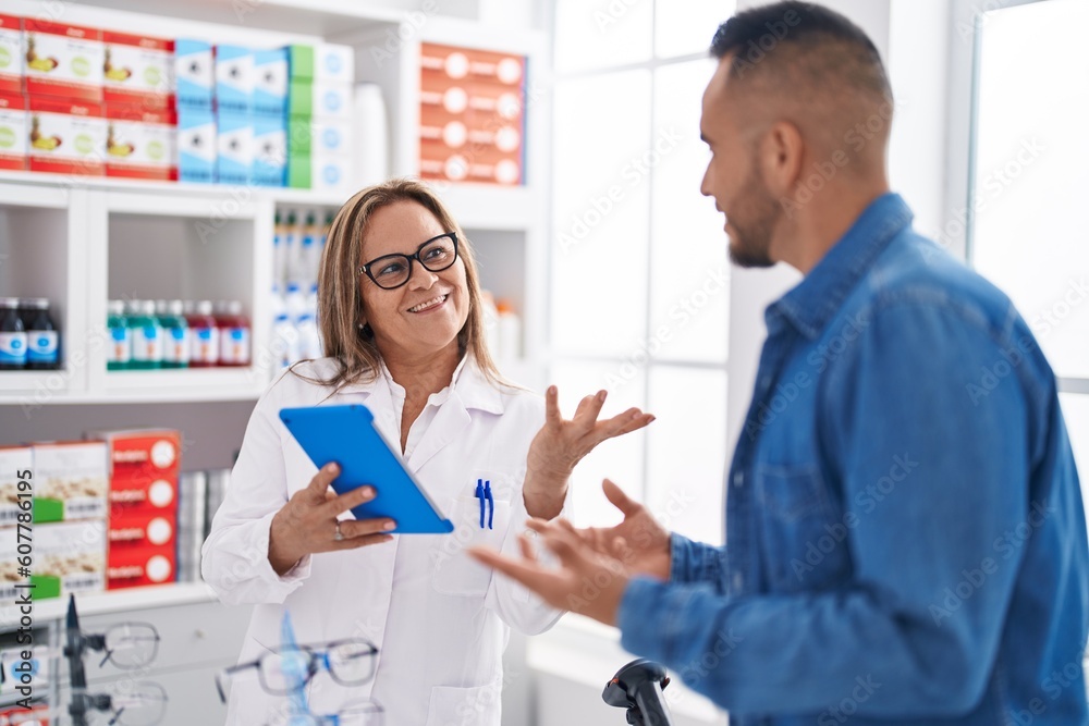 Man and woman pharmacist smiling confident using touchpad at pharmacy