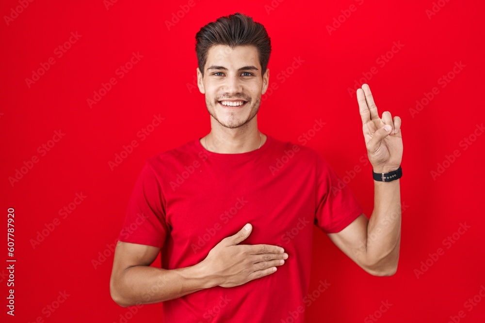 Naklejka premium Young hispanic man standing over red background smiling swearing with hand on chest and fingers up, making a loyalty promise oath