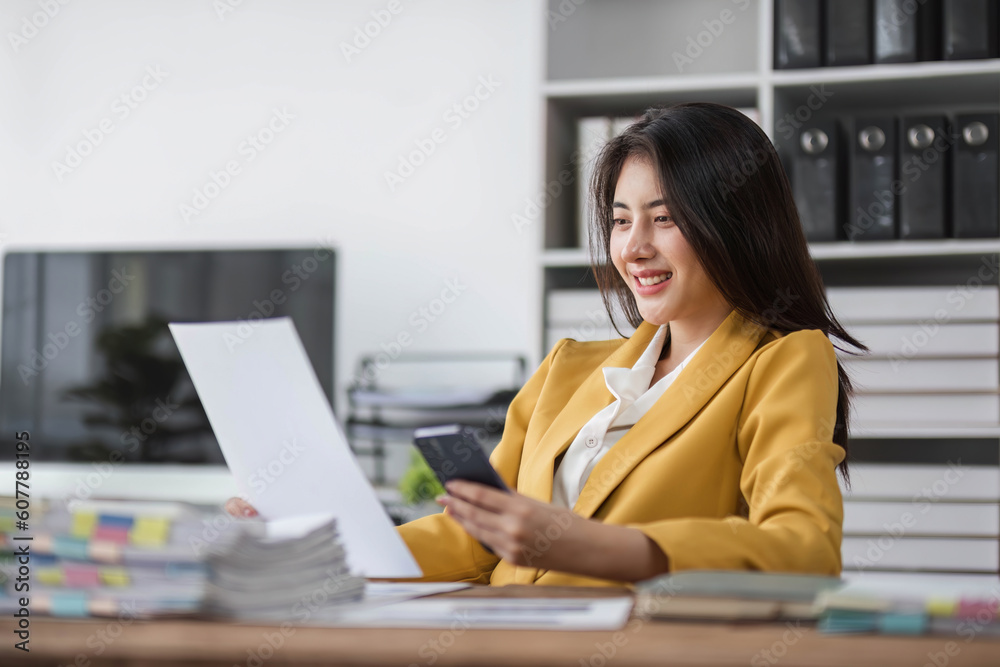 Young busy asian business woman talking on phone working in modern office. Asian businesswoman company sales client manager wearing suit making call on cellphone sitting at workplace. Young busy asian business woman talking on phone working in modern office. Asian businesswoman company sales client manager wearing suit making call on cellphone sitting at workplace.