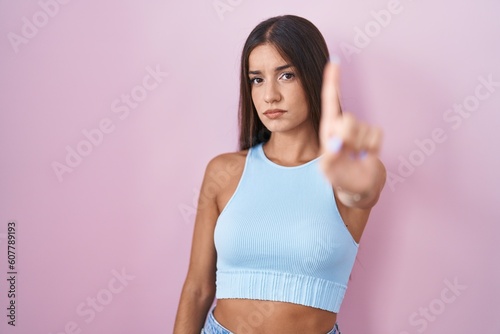 Young brunette woman standing over pink background pointing with finger up and angry expression, showing no gesture © Krakenimages.com