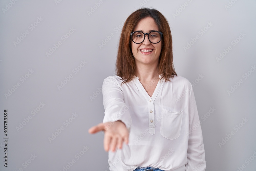 Brunette woman standing over white isolated background smiling cheerful offering palm hand giving assistance and acceptance.