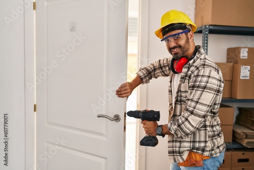 Young hispanic man worker smiling confident repairing door at home