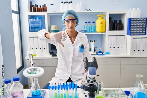 Brunette woman working at scientist laboratory looking unhappy and angry showing rejection and negative with thumbs down gesture. bad expression.
