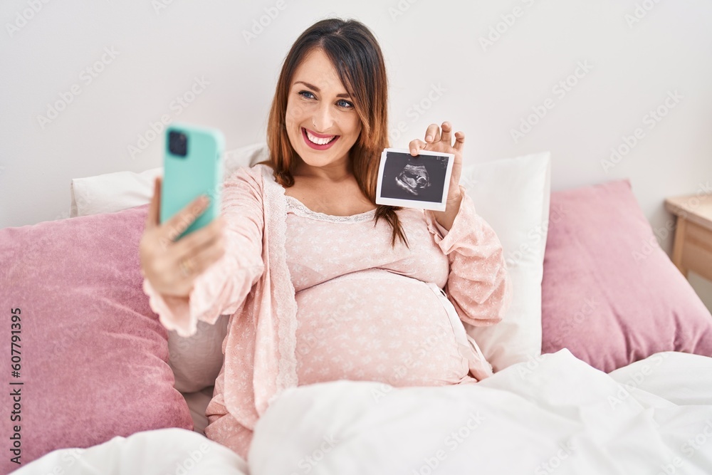 Young pregnant woman make selfie by smartphone holding ecography at bedroom Young pregnant woman make selfie by smartphone holding ecography at bedroom