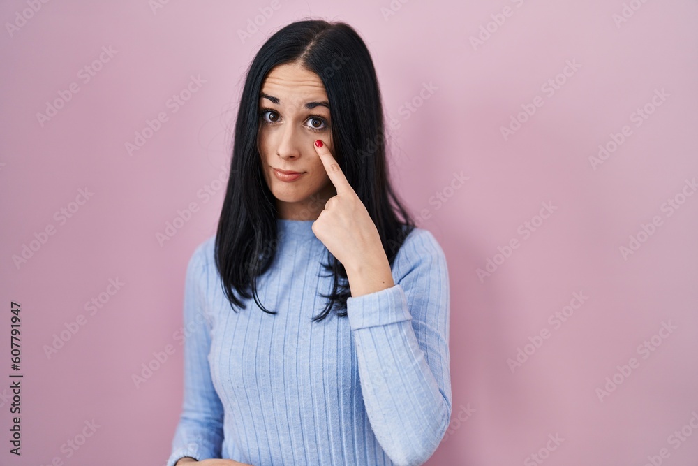 Hispanic woman standing over pink background pointing to the eye watching you gesture, suspicious expression Hispanic woman standing over pink background pointing to the eye watching you gesture, suspicious expression