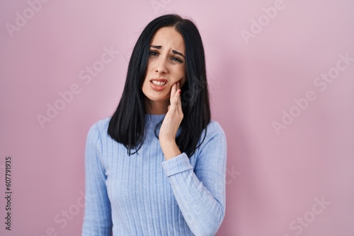 Hispanic woman standing over pink background touching mouth with hand with painful expression because of toothache or dental illness on teeth. dentist