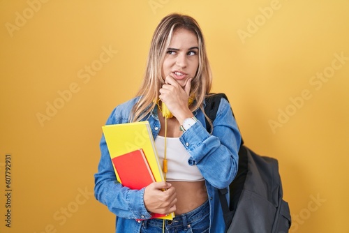 Young blonde woman wearing student backpack and holding books thinking worried about a question, concerned and nervous with hand on chin