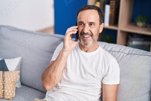 Middle age man talking on smartphone sitting on sofa at home