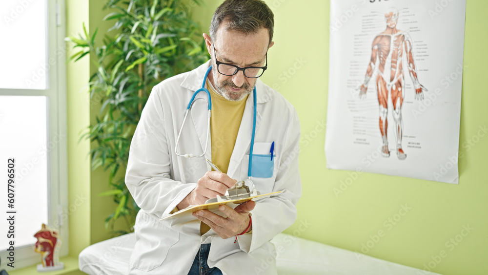 Middle age man doctor writing document on clipboard at clinic Middle age man doctor writing document on clipboard at clinic