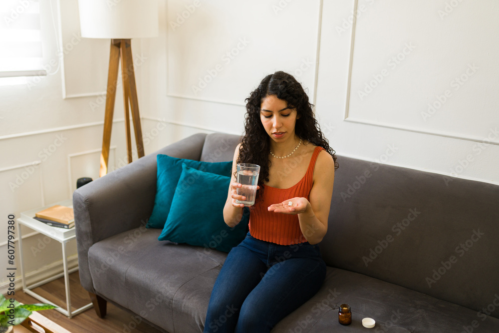 Sick woman taking her prescription pills in the living room Sick woman taking her prescription pills in the living room