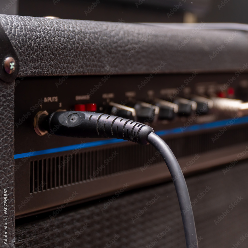 Plug jack with cable plugged into a black guitar combo amplifier Plug jack with cable plugged into a black guitar combo amplifier
