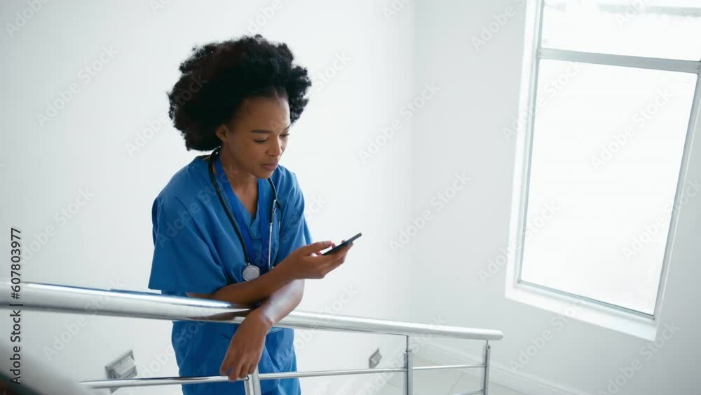 Portrait of female doctor or nurse wearing scrubs looking at mobile phone on hospital stairs - shot in slow motion Portrait of female doctor or nurse wearing scrubs looking at mobile phone on hospital stairs - shot in slow motion